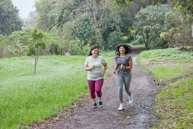Two women jogging side by side on a grassy park trail