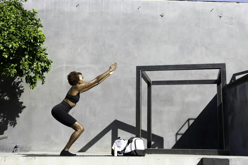 A woman doing a bodyweight squat against a concrete wall outdoors