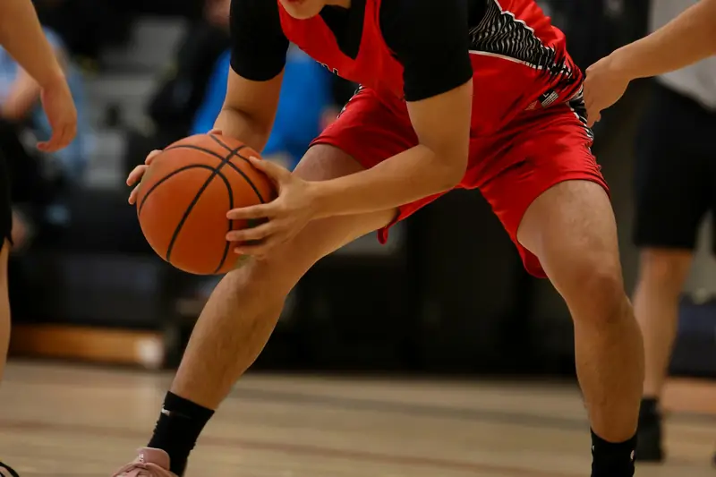 A player in a low stance, holding the ball at knee height on an indoor court