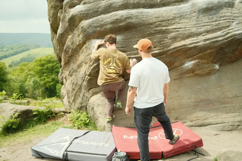 Two boulderers at an outdoor sandstone boulder with crash pads laid out below