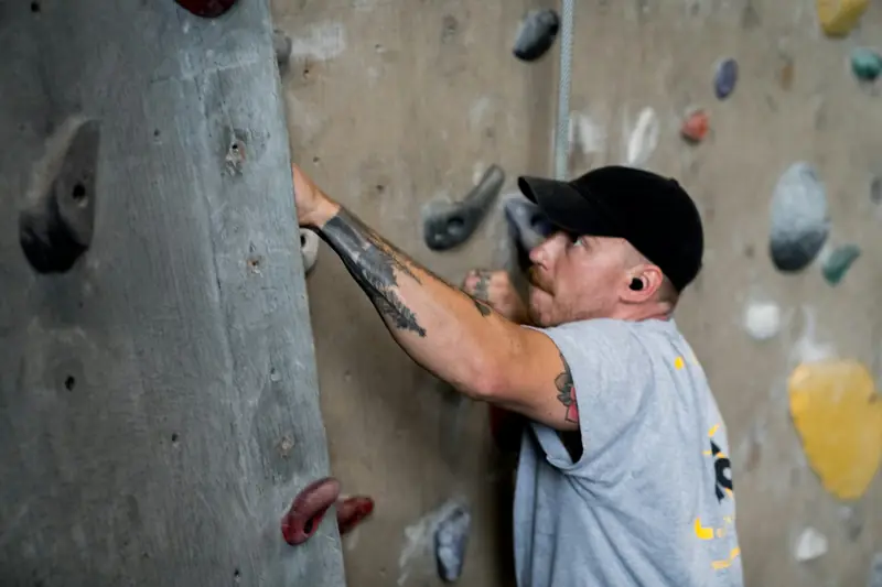 A climber in a cap gripping a hold on an indoor wall