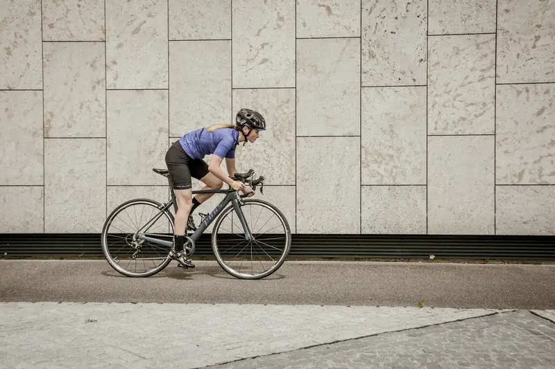 A rider on a road bike seen from the side, riding past a pale stone wall