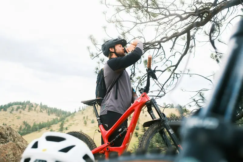 A rider drinking from a bottle beside his bike on a hillside trail