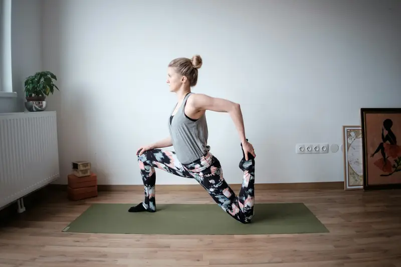 A woman doing a kneeling hip and thigh stretch on a mat at home
