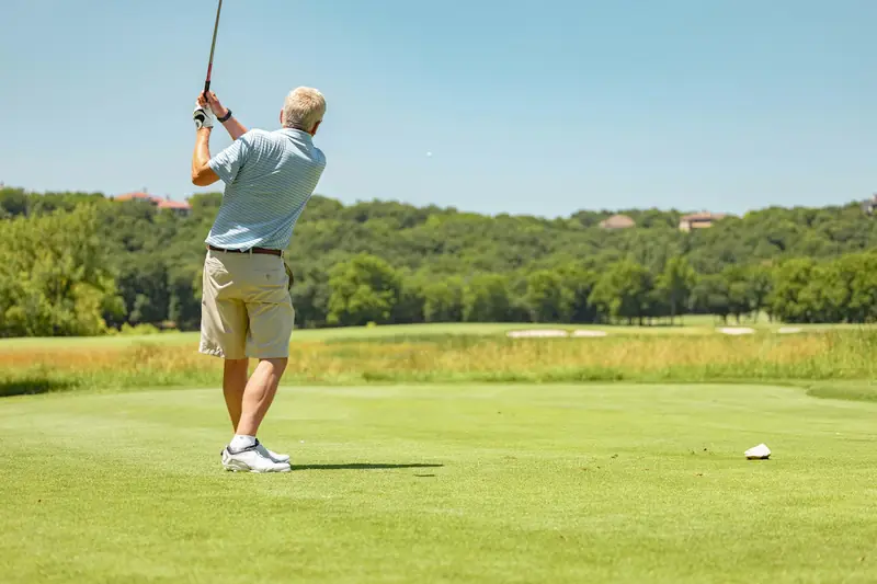 An older golfer finishing a tee shot on a sunny course