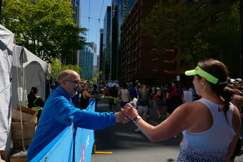 A runner taking a cup of water from a volunteer at a race aid station