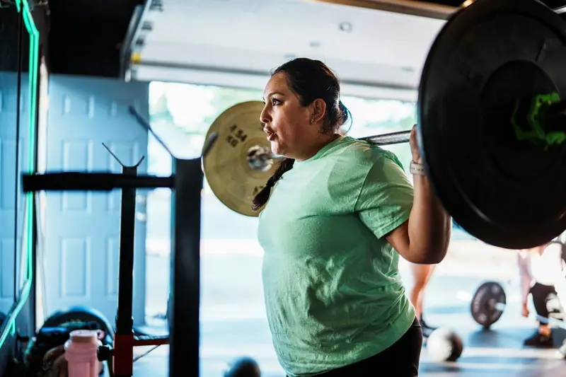 A woman lifting a loaded barbell onto her shoulders for a squat in a gym
