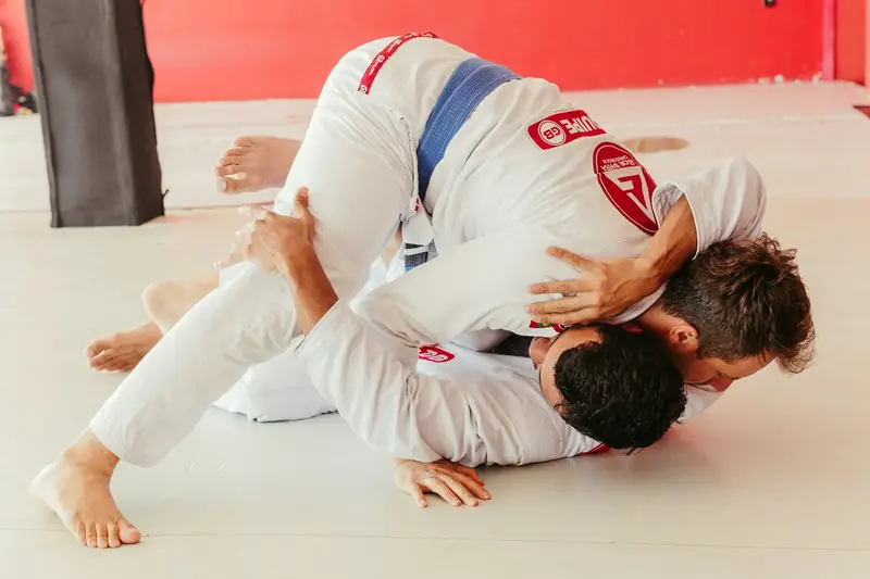 Two people in white jiu-jitsu gis grappling on the mat