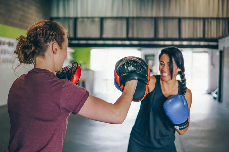 A woman in boxing gloves throwing a punch at focus pads held by a training partner