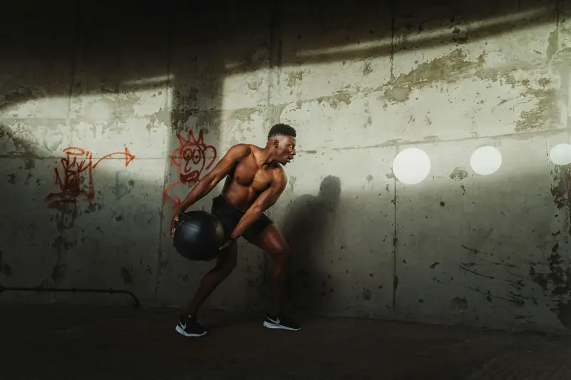 A man doing a one-arm kettlebell swing against a concrete wall