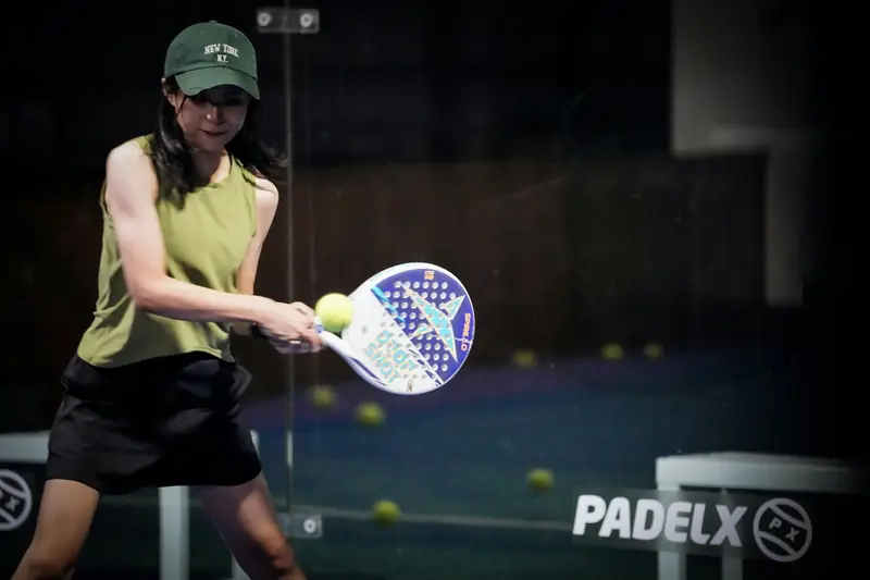 A padel player hitting the ball low to high on an indoor court