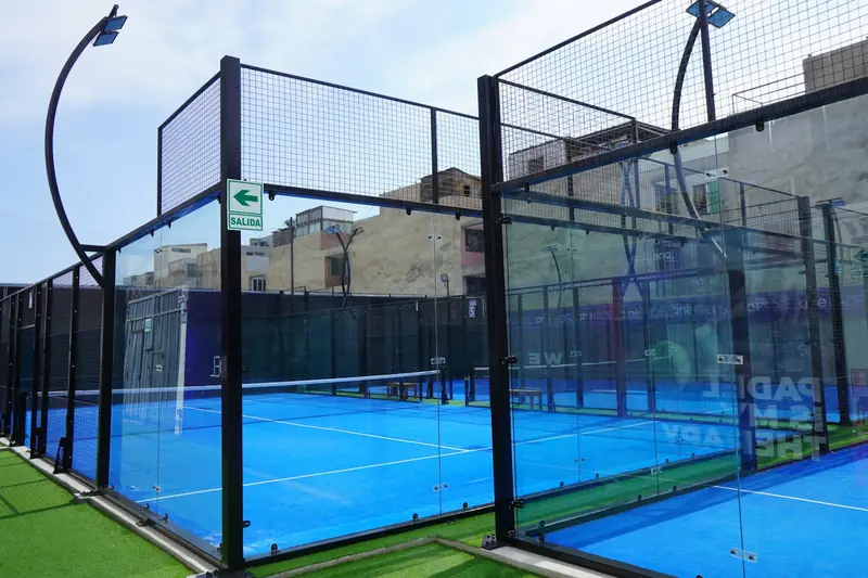 An outdoor padel court with glass back walls and a mesh fence