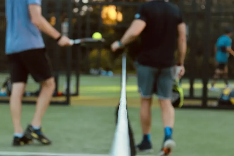 Two padel players at the net during a rally, seen through the net