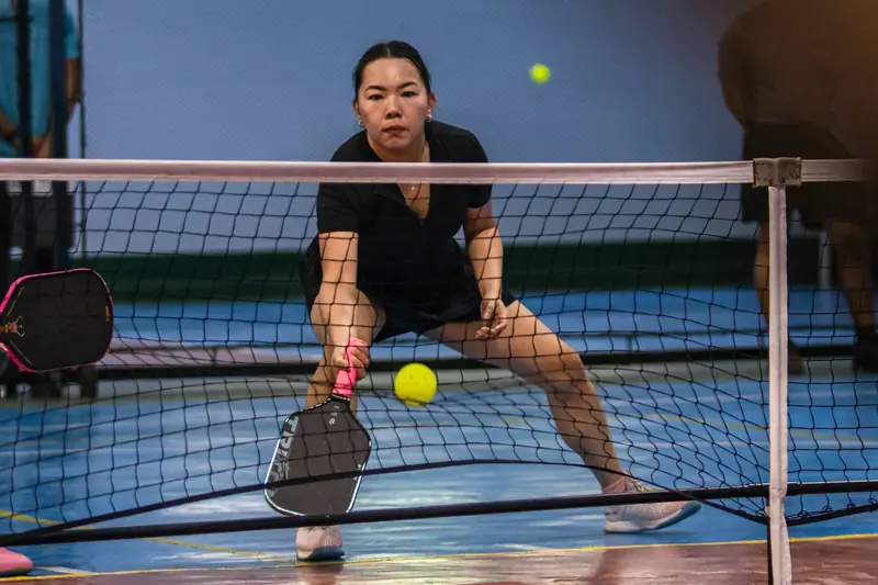 A player crouched low at the net, about to play a soft shot just over it