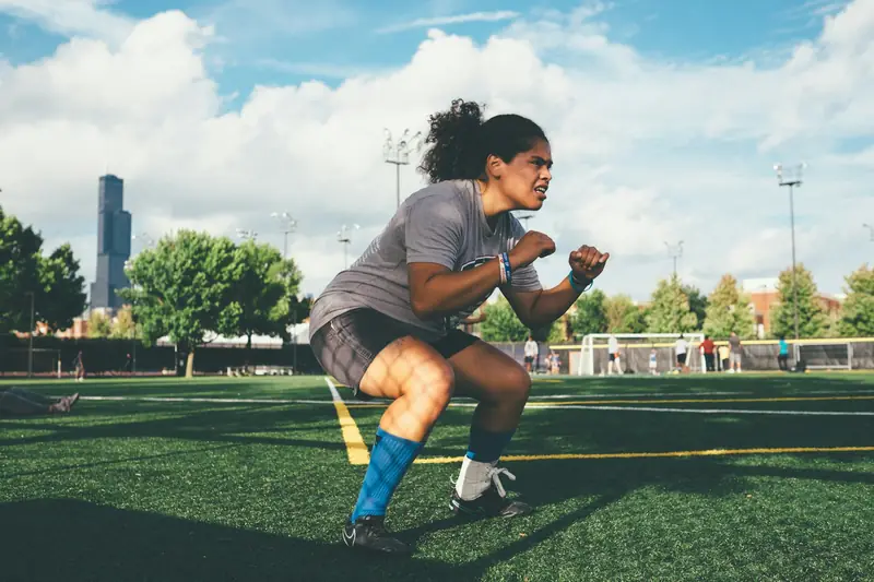 A woman holding a low, athletic squat on a sports field