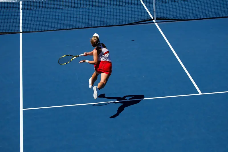 A tennis player stretching wide on a blue hard court to reach a forehand