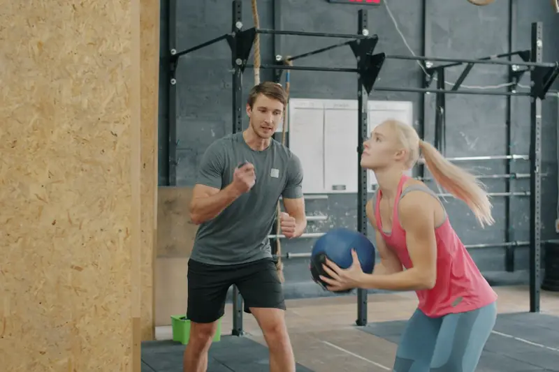 A trainer coaching a woman as she holds a medicine ball in a gym